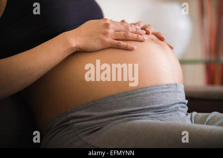 Baby bump, immagine di un 8 mese di gravidanza donna seduta su un divano, appoggiando le mani sulle sue baby bump pancia. Foto Stock