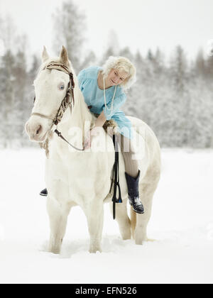 Donna attraente indossando abiti blu e lei in sella ad un cavallo bianco Foto Stock