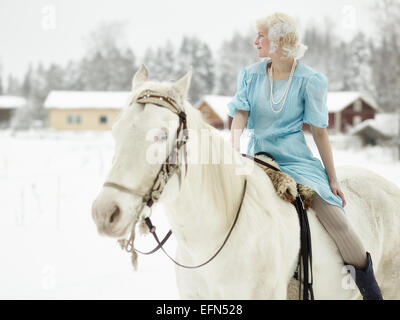 Donna attraente indossando abiti blu e lei in sella ad un cavallo bianco Foto Stock