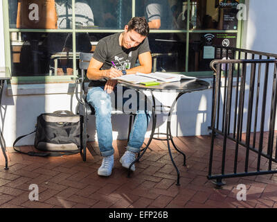 Una ventina di qualcosa di collegio maschile studente studi presso una tabella su un patio esterno una caffetteria a Santa Barbara, California. Foto Stock