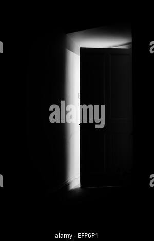 Luce proveniente attraverso una porta aperta in una stanza buia la notte. Monocromatico Foto Stock