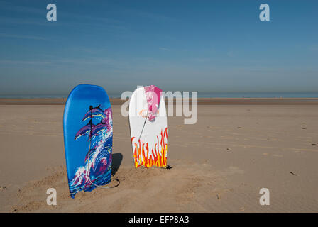 Due pannelli di corpo piantato nella sabbia con l'Oceano Atlantico mare lontano in attesa di marea ad entrare nella rosa di essiccazione rash vest Foto Stock