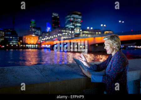 Coppia imprenditrice utilizzando digitale compressa sul Tamigi waterfront di notte, Londra, Regno Unito Foto Stock