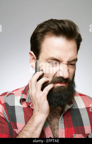 Studio Ritratto di giovane uomo di graffiare la barba ricoperta Foto Stock