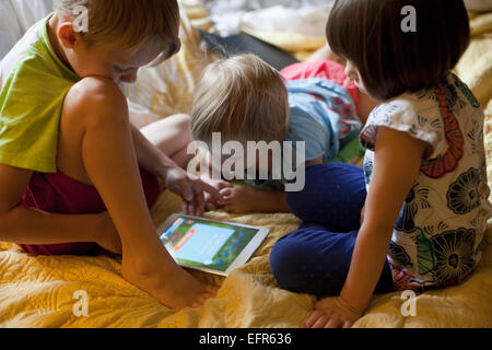 Tre bambini relax su letto tramite tavoletta digitale Foto Stock