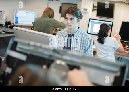 Un uomo seduto a un computer in un negozio di riparazione. Foto Stock