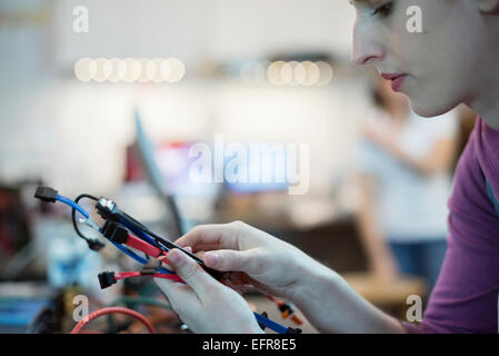 Una giovane donna utilizzando i cavi di collegamento e porta USB in un computer repair shop. Foto Stock