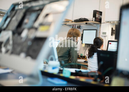 La riparazione di un computer Shop. Due persone sedute utilizzando degli schermi e i monitor dei computer in varie fasi della riparazione. Foto Stock