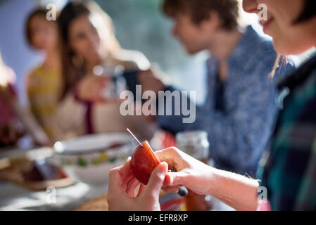 Un gruppo di persone sedute a un tavolo a mangiare e a chiacchierare. Una donna per affettare un apple. Foto Stock