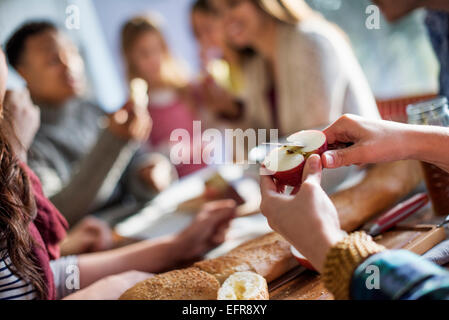 Un gruppo di persone sedute a un tavolo a mangiare e a chiacchierare. Una donna per affettare un apple. Foto Stock