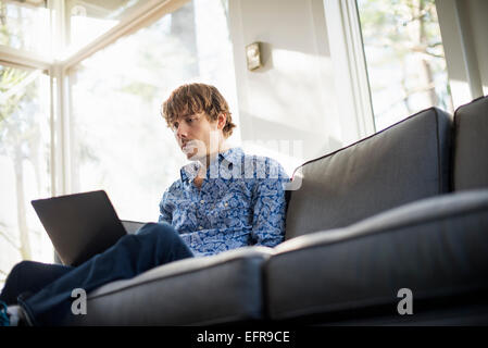 Basso angolo di visione di un uomo seduto su un divano guardando al suo computer portatile. Foto Stock