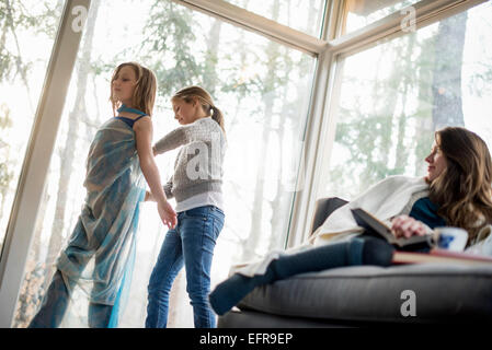 Due ragazze in piedi in un salotto, vestirsi, una donna seduta su un divano, guardando. Foto Stock