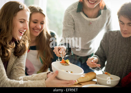 Quattro persone sedute e in piedi in una tabella di una donna che serve cibo in una ciotola. Foto Stock