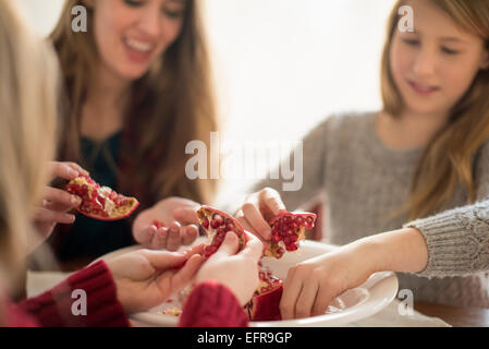 Due ragazze e una donna seduta al tavolo, picking chicchi di un melograno. Foto Stock