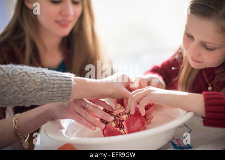 Due ragazze e una donna seduta al tavolo, picking chicchi di un melograno. Foto Stock