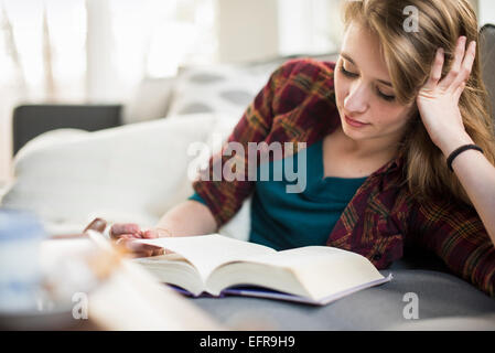 Giovane donna seduta su un divano, la lettura di un libro. Foto Stock