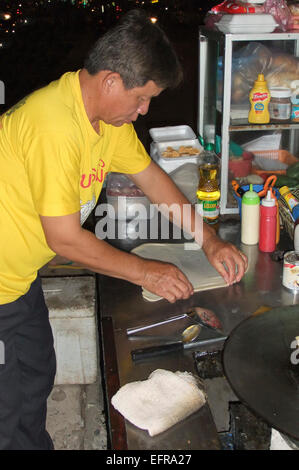 Ritratto verticale di un venditore ambulante occupato rendendo i pancake freschi sul ciglio della strada in Laos. Foto Stock