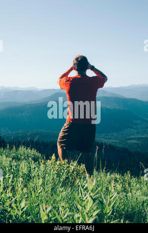 Un uomo in piedi su un crinale montuoso, scattare una fotografia di paesaggio e la valle boscosa. Foto Stock