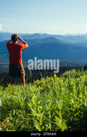 Un uomo in piedi su un crinale montuoso, scattare una fotografia di paesaggio e la valle boscosa. Foto Stock