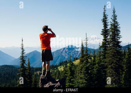 Un uomo in piedi su un crinale montuoso, scattare una fotografia di paesaggio. Foto Stock