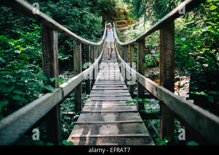 Uomo che cammina attraverso piccolo ponte pedonale in lussureggianti foreste pluviali temperate, Oswald West SP O Foto Stock