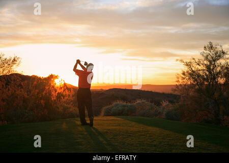 Il Golfer prendendo uno swing sul tee affacciato sul paesaggio di un campo da golf al crepuscolo in Arizona. Foto Stock
