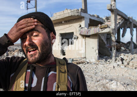 Kobane, Siria. 6 febbraio, 2015. Un Kuridsh fighter del YPG sorge di fronte a una casa distrutta in Kobane, Siria, 6 febbraio 2015. I pesanti combattimenti negli ultimi mesi tra i curdi e Stato islamico (SI) fighters hanno girato di ampie parti della città di Kobane in un campo di detriti. Foto: Sebastian Backhaus/dpa - nessun filo SERVICE -/dpa/Alamy Live News Foto Stock