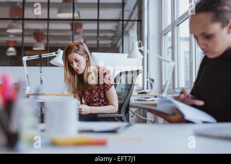 Immagine della giovane donna occupato a lavorare alla sua scrivania con un collega lettura una relazione di fronte. Foto Stock