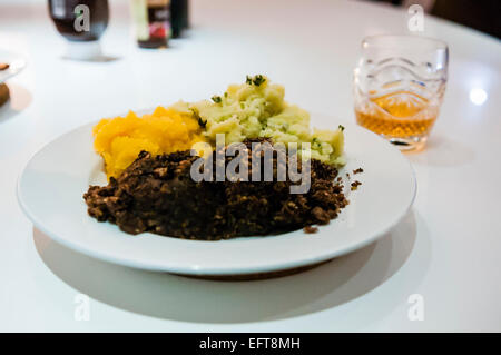 Haggis, Neeps (rape) e tatties (patate) con un bicchiere di whisky su ustioni di notte. Foto Stock