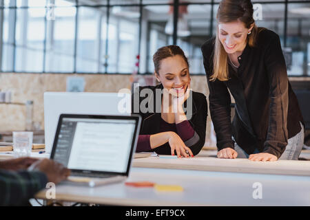 Due giovani donna in ufficio a lavorare su un nuovo design creativo. Diversi team di professionisti alla ricerca di un documento sorridente. Foto Stock