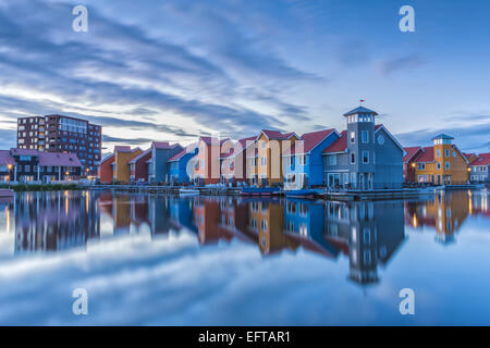 Luminose colorate case di legno riflettendo in acqua con un cielo blu in Olanda al tramonto Foto Stock