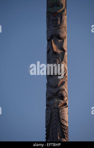 Un sole che illumina un totem pole con la luna nuova in background, Victoria, British Columbia, Canada. Foto Stock