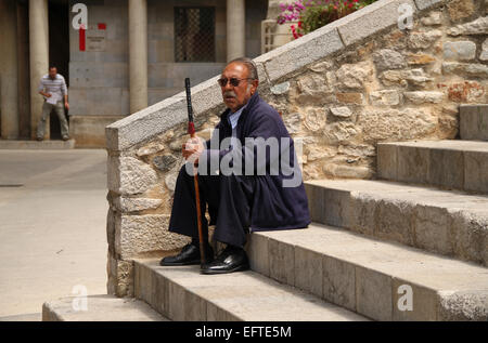 Il vecchio uomo seduto con bastone sui passi nella città vecchia di Girona (Gerona), Catalogna, Spagna Foto Stock