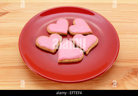 5 a forma di cuore biscotti ghiacciata su una targhetta rossa per il giorno di San Valentino, su di un tavolo di legno Foto Stock