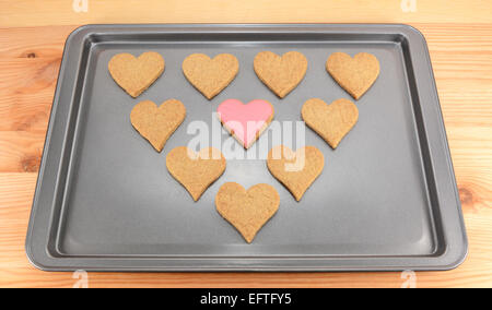 Pianura a forma di cuore i biscotti su una teglia da forno con una rosa di biscotto glassato al centro Foto Stock