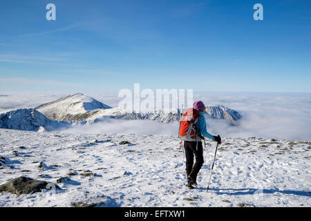 Escursionista solitario sulla penna Yr Ole Wen ridge con Elidir Fawr, Mynydd Perfedd e Carnedd y Filiast cime sopra basse nubi in inverno la neve. Snowdonia Wales UK Foto Stock