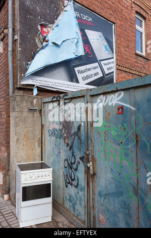 Un vecchio fornello elettrico si trova nella strada accanto ad una porta di metallo coperto di graffiti e al di sotto di un peeling pubblicità Affissioni Foto Stock