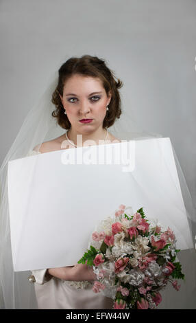 Piuttosto giovane sposa con un broncio bridezilla come azienda di espressione segno bianco e bouquet di rose rosa Foto Stock