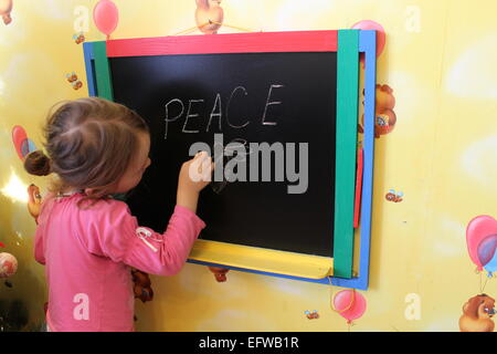 Piccola ragazza scrive sulla lavagna parola pace Foto Stock