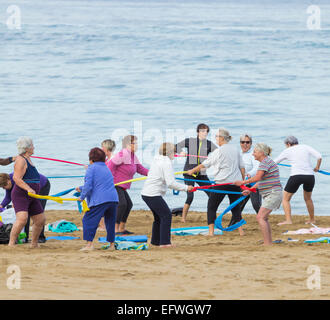 Anziani spagnolo delle donne che esercitano con bande di resistenza sulla spiaggia in Spagna Foto Stock