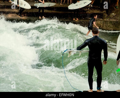 Surfers pratica in Englischer Garten di Monaco di Baviera su onde artificiali a Eisbach, piccolo fiume che attraversa il parco Foto Stock