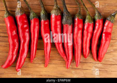 Peperoncino rosso giacente in una fila su un sfondo di legno Foto Stock