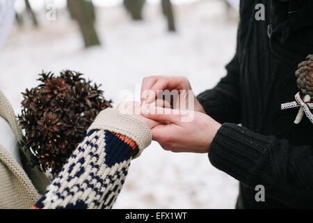 Lo sposo di mettere l'anello di matrimonio su sposa il dito in corrispondenza di inverno di nozze Foto Stock