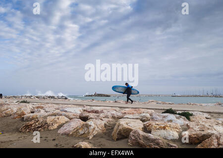 Surfer cammina su un molo di pietra a cavalcare le onde durante le giornate di cattivo tempo e di onde alte, mare mosso, Fuengirola, Andalusia, Spagna. Foto Stock
