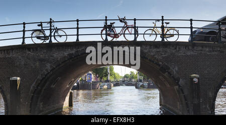 Biciclette incatenato ad una arcata in mattoni ponte su un canale in Amsterdam, Paesi Bassi Foto Stock