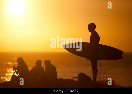 Il surfer che trasportano le tavole da surf sulla spiaggia al tramonto, Taghazout, Marocco Foto Stock