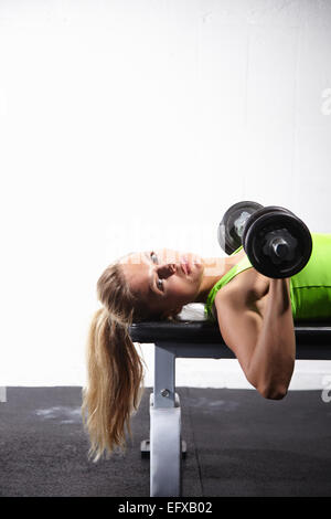 Giovane donna sdraiata sulla panca training con bar campana in palestra Foto Stock