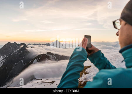 Giovane uomo fotografare sunrise sullo smartphone, Alpi Bavaresi, Oberstdorf, Baviera, Germania Foto Stock