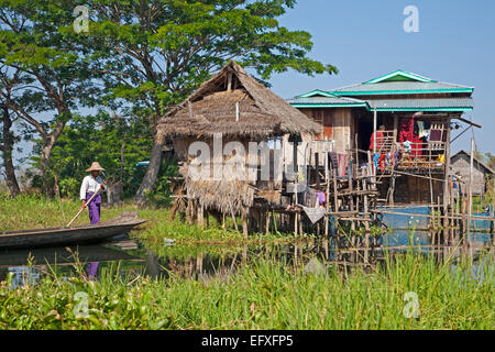 Intha uomo in proa a borgo lacuale con bambù case su palafitte in Lago Inle, Nyaungshwe, Stato Shan, Myanmar / Birmania Foto Stock