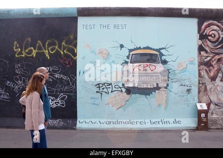 Giovane oltrepassando Birgit Kinder's artwork di Trabant vettura lo scoppio attraverso la parete quinto aggiornamento di illustrazione con ulteriori graffit Foto Stock